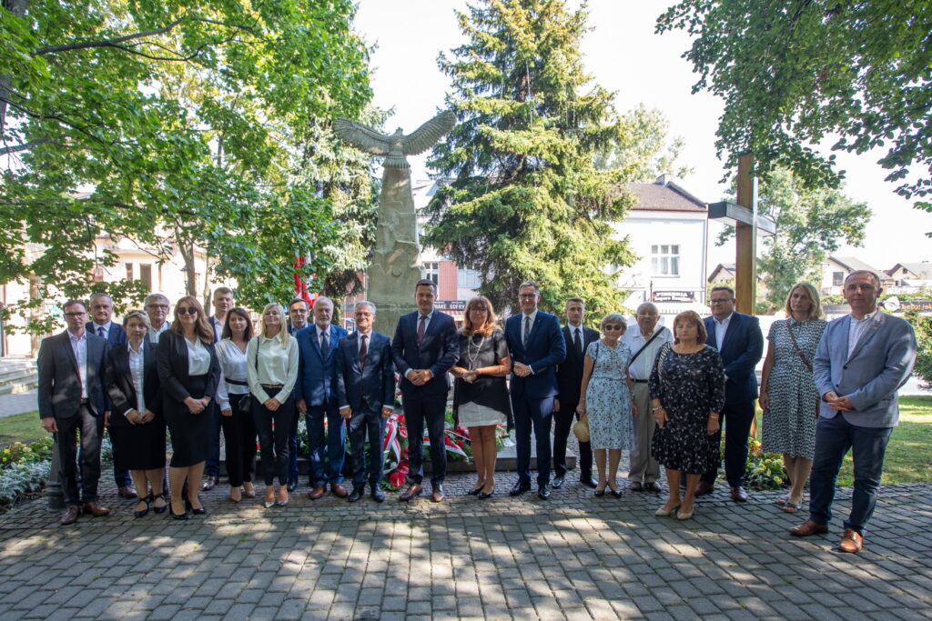 Uczestnicy rocznicowej uroczystości. W tle pomnik zwieńczony orłem