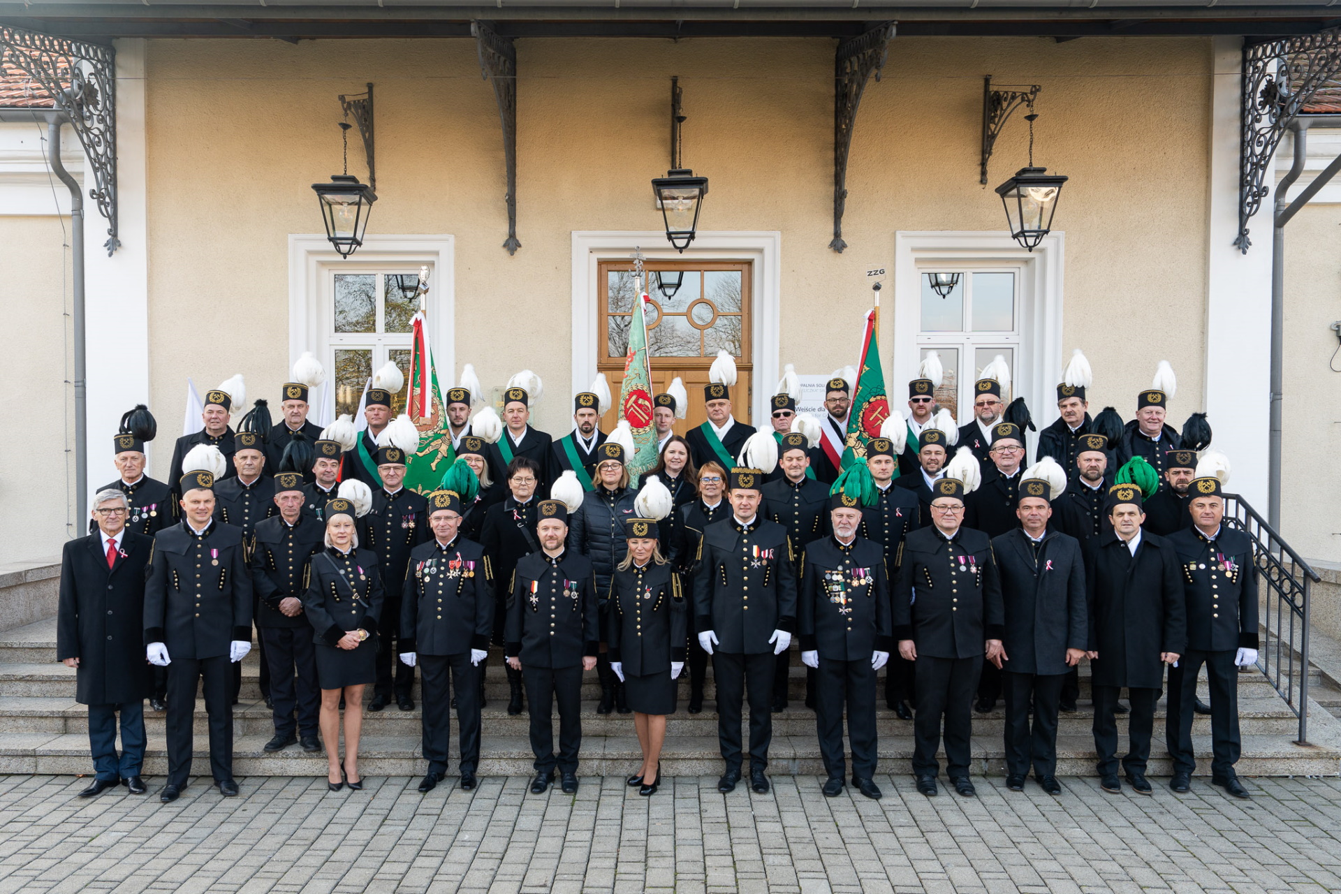 Górnicy w galowych mundurach na stopniach widodących do budynku szybu Daniłowicza. Pamiątkowe zdjęcie